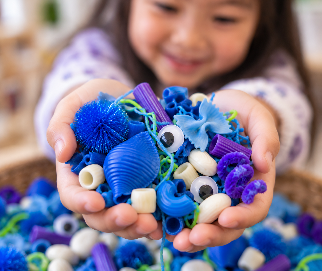 Preschool child holding blue and purple monster sensory-bin materials