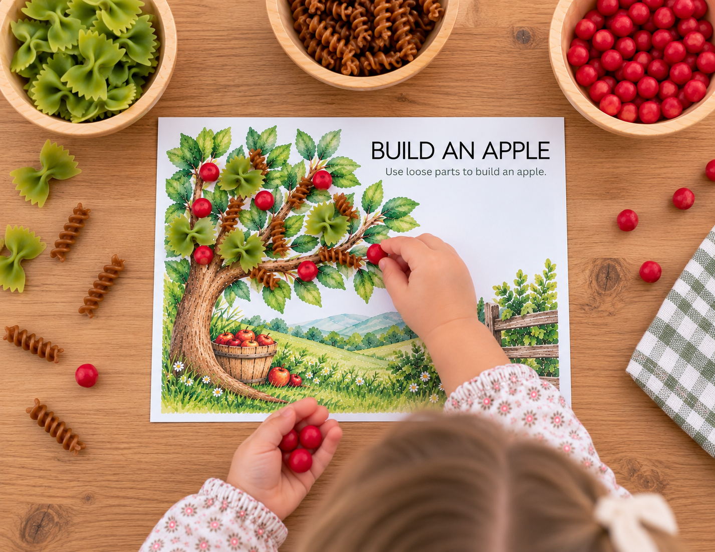 Child using dyed pasta and loose parts to build an apple on a Play Beyond Pasta activity mat