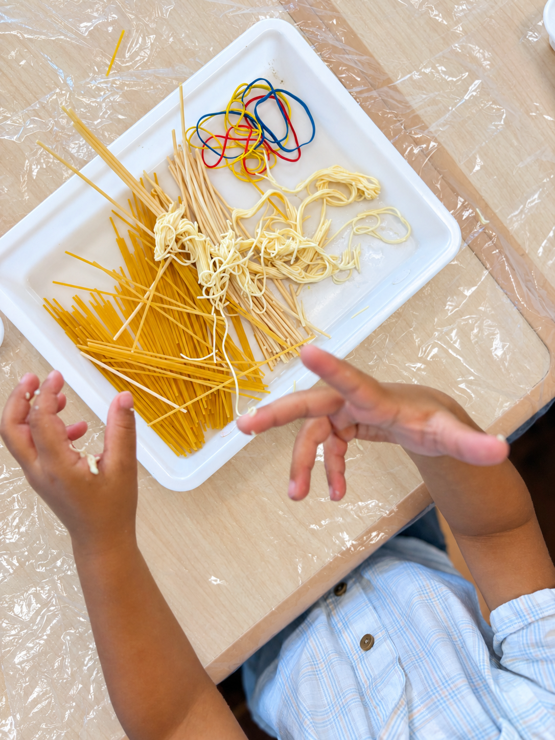 A preschooler using colorful bands to gather three textures of spaghetti into bundles