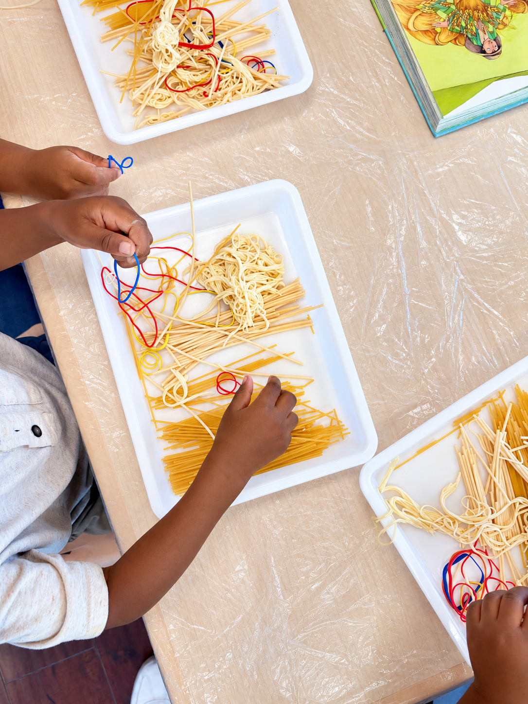 Three preschool activity trays with different spaghetti textures and colorful bands